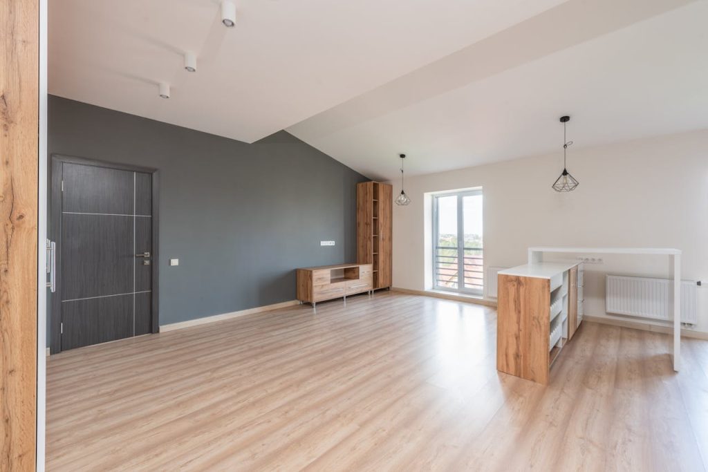 brown-wooden-table-in-the-room-8146316 Spacious modern living room featuring wooden flooring, gray accent wall, and natural light.
