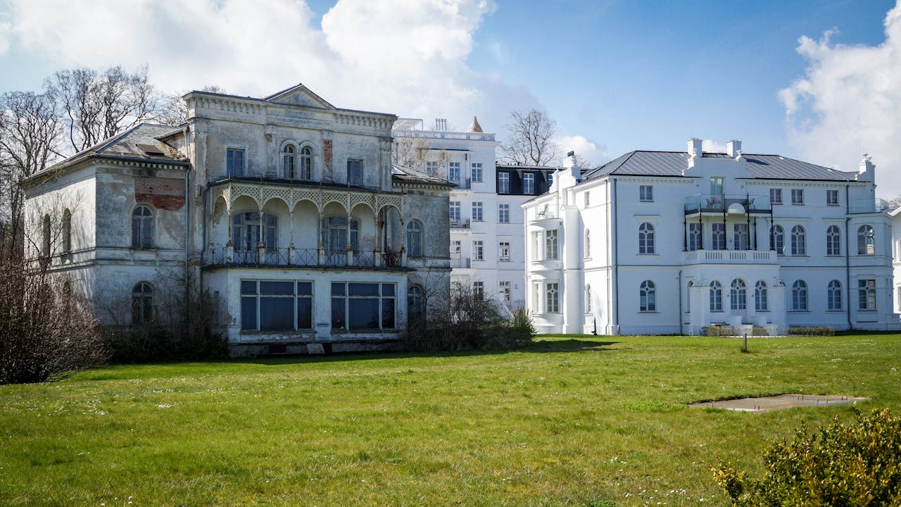 An old mansion contrasts against a modern building in a sunny landscape.